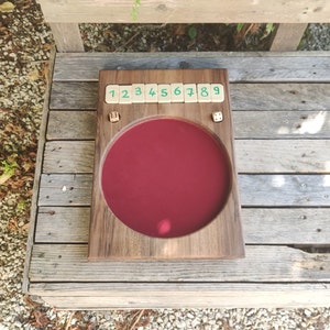 May include: A wooden game board with a red felt playing surface and numbered tiles. The tiles are labelled 1 through 9. There are two dice on the board.
