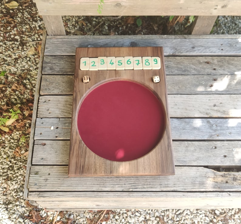 May include: A wooden game board with a red felt playing surface and numbered tiles. The tiles are labelled 1 through 9. There are two dice on the board.