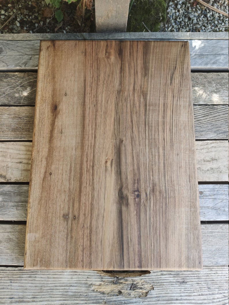 May include: A large, rectangular wooden chopping board with a natural wood grain finish. The board has a dark brown colour and is made of solid wood.