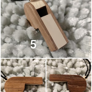 K&ouml;nnte beinhalten: Ein h&ouml;lzerner Pfeifenanh&auml;nger mit zweifarbigem Design aus hellem und dunkelbraunem Holzmaserung, einer schwarzen Kordel und der auf der Seite aufgedruckten Zahl 5. Die Pfeife hat ein rechteckiges Mundst&uuml;ck und einen abgerundeten K&ouml;rper.