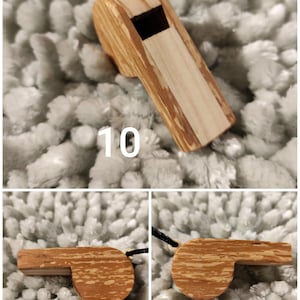 K&ouml;nnte beinhalten: Eine Holzpfeife mit einer hellbraunen und beigen Holzmaserung und einer schwarzen Kordel, die an einem cremefarbenen Verbindungsst&uuml;ck befestigt ist. Die Pfeife hat eine rechteckige Schallkammer und eine glatte Oberfl&auml;che. Die Zahl 10 ist zu sehen.
