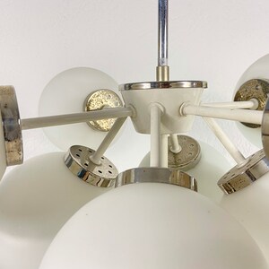 May include: A white ceiling light fixture with multiple globe-shaped shades. The fixture has a chrome finish and a white center piece.