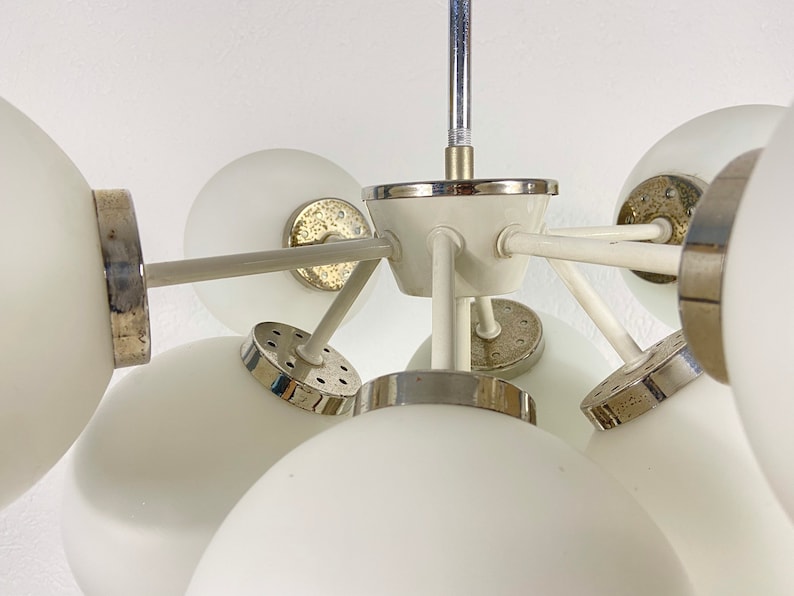 May include: A white ceiling light fixture with multiple globe-shaped shades. The fixture has a chrome finish and a white center piece.