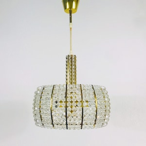 May include: A gold-toned chandelier with a cylindrical shape, featuring a design of clear crystal beads arranged in a geometric pattern.