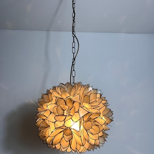 Op de afbeelding: Een bolvormige hanglamp met een bloemenontwerp. Het licht hangt aan een ketting en heeft een warm, gloeiend licht dat uit de bloemachtige bloembladen komt. De armatuur heeft een neutrale kleur.