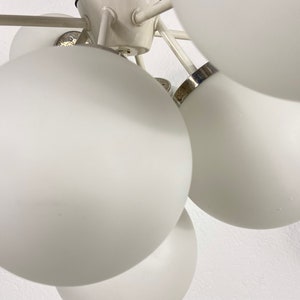 May include: A white ceiling light fixture with multiple round, white glass shades. The fixture has a silver metal frame and is designed to be hung from the ceiling.
