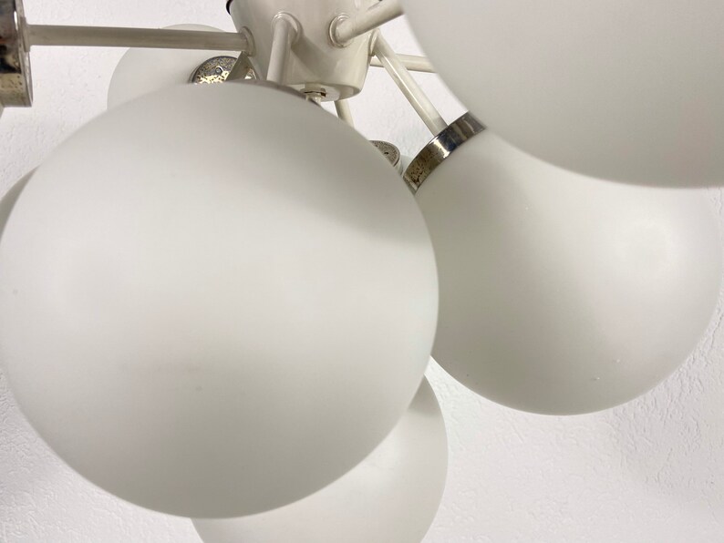May include: A white ceiling light fixture with multiple round, white glass shades. The fixture has a silver metal frame and is designed to be hung from the ceiling.