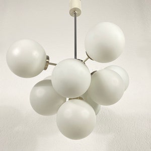 May include: A white ceiling light fixture with six round white glass shades. The shades are connected by metal rods and the fixture is suspended from the ceiling by a single metal rod.