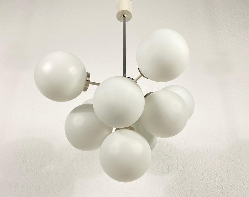 May include: A white ceiling light fixture with six round white glass shades. The shades are connected by metal rods and the fixture is suspended from the ceiling by a single metal rod.