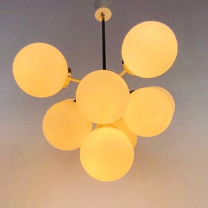 May include: A modern chandelier with six white glass globes, each with a warm, glowing light. The chandelier has a black metal frame and gold accents.