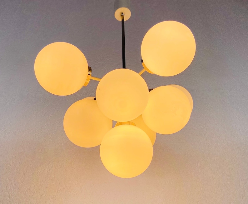 May include: A modern chandelier with six white glass globes, each with a warm, glowing light. The chandelier has a black metal frame and gold accents.