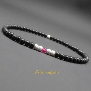 Peut inclure: Un bracelet en perles noires avec une perle d'accent rose et argent. Le bracelet est sur une surface grise. "Androgeen" est écrit en lettres dorées sous le bracelet.