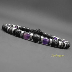 Pode incluir: Pulseira de contas pretas com pedras de lava, pedras de ametista roxas e detalhes metálicos prateados. A pulseira é enfiada em um cordão preto. A palavra "Androgeen" está na imagem, em um fundo cinza.
