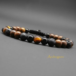 Peut inclure: Un bracelet composé de perles en bois brun, de lave noire, d'œil de tigre et d'onyx noir. Le bracelet est attaché avec un cordon noir.