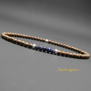Könnte beinhalten: Ein braunes Perlenarmband mit einer Reihe blauer Edelsteinperlen und silbernen Abstandshaltern. Das Armband liegt auf einem grauen Hintergrund und das Wort "Androgeen" ist in Gelb unter dem Armband geschrieben.