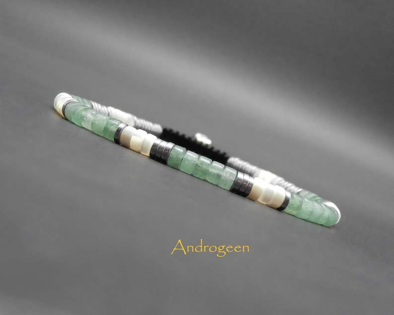 May include: A green, white, and black beaded bracelet with a silver clasp. The bracelet is made with small, square-shaped beads.