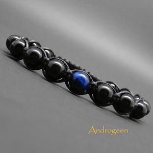 Peut inclure: Bracelet en perles noires avec une pierre de œil de tigre bleu. Le bracelet est fait avec un cordon noir et présente un design noué.