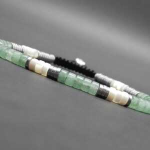 May include: A green and white beaded bracelet with a black cord. The bracelet features green jade beads, white shell beads, and silver metal beads.
