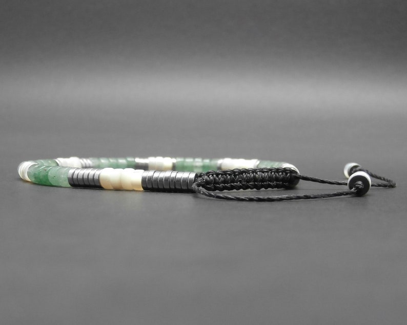 May include: A green, white, and black beaded bracelet with a black cord and white bead accents.
