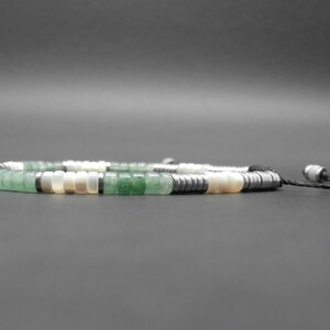 May include: A green, white, and black beaded necklace with a black cord and silver toggle clasp.