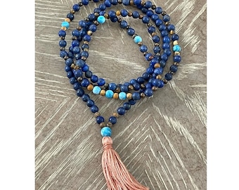 May include: A blue and brown beaded necklace with a pink tassel. The necklace is made of lapis lazuli, tiger's eye, and turquoise beads.