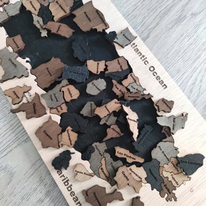 May include: A wooden puzzle map of Puerto Rico with the names of each municipality labeled. The puzzle pieces are arranged in the shape of the island, with the Atlantic Ocean to the north and the Caribbean Sea to the south.