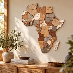 Könnte beinhalten: Eine mehrschichtige Holzwandkarte von Afrika in verschiedenen Braun-, Beige- und Grautönen. Die Karte zeigt Ländernamen und das Wort SAHARA in der nördlichen Region. Sie ist an einer Wand über einem Holzschrank mit Büchern montiert.