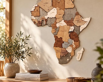 May include: A multi-layered wooden wall map of Africa featuring various shades of brown, tan, and grey. The map displays country names and the word SAHARA across the northern region. It is mounted on a wall above a wooden cabinet with books.