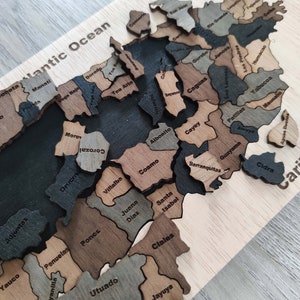 May include: A wooden puzzle map of Puerto Rico with the names of each municipality labeled. The puzzle pieces are arranged to form the shape of the island. The puzzle is made of different shades of brown wood.