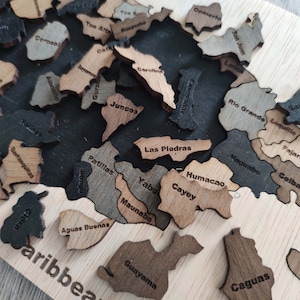 May include: A wooden puzzle map of Puerto Rico with the names of different cities and towns labeled on each piece. The puzzle pieces are arranged in a way that resembles the shape of the island. The puzzle is set against a black background.