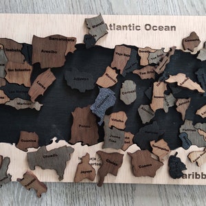 May include: A wooden jigsaw puzzle of Puerto Rico, featuring the names of each municipality. The puzzle pieces are arranged to form the shape of the island, with the Atlantic Ocean and Caribbean Sea labeled at the top and bottom. The puzzle is made of different shades of brown wood.