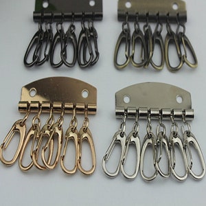 May include: Four keychains with five metal hooks each. The keychains are in four different finishes: black, antique brass, gold, and silver.