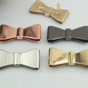 May include: Four metal bow-shaped decorative embellishments in silver, gold, rose gold, and gunmetal.