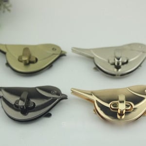 May include: Four metal bird-shaped clasps in gold, silver, and black. Each clasp has a central locking mechanism. The bird's body is rounded, with a pointed tail and a small beak. These clasps are likely for bags or other craft projects.