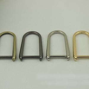 Könnte beinhalten: Vier D-Ringe aus Metall in verschiedenen Ausführungen: Gold, Silber, Schwarz und Antikmessing. Die Ringe sind alle gleich groß und haben die gleiche Form und eine glatte, polierte Oberfläche.