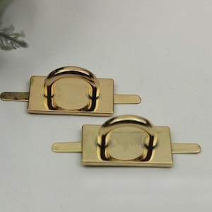 May include: Two gold-toned metal rings with rectangular plates attached. The rings are designed for attaching to bags or other items.