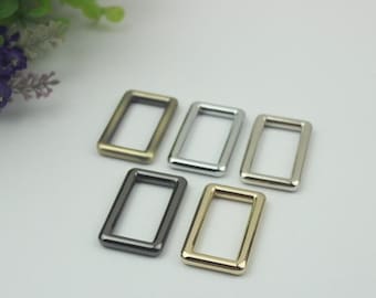 May include: Five metal D-rings in different finishes: gold, silver, brass, black, and nickel. The rings are all the same size and shape.