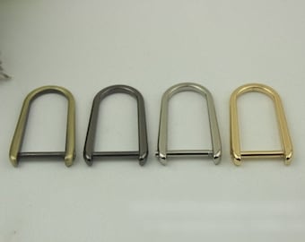 May include: Four metal D-rings in different finishes: gold, silver, black, and antique brass. The rings are all the same size and shape, and they have a smooth, polished finish.