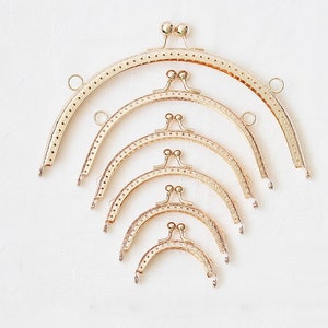 Könnte beinhalten: Satz mit sechs goldfarbenen Metall-Taschenrahmen in verschiedenen Größen. Die Rahmen sind für die Verwendung bei der Herstellung von Handtaschen und Taschen gedacht.