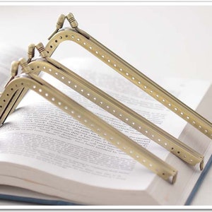 Könnte beinhalten: Drei goldene Metalltaschenrahmen mit gepunktetem Design. Die Rahmen liegen auf einem Buch.