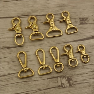 May include: A set of ten gold-toned metal clasps or swivel hooks. The clasps are of various sizes and shapes, with some featuring a decorative design.