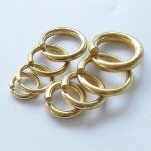 May include: A set of six gold-colored metal jump rings of varying sizes. The rings are interlocked and arranged in a circular pattern.