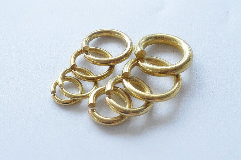 May include: A set of six gold-colored metal jump rings of varying sizes. The rings are interlocked and arranged in a circular pattern.