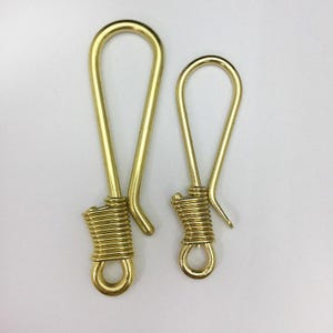 Può includere: Due portachiavi in ottone. I portachiavi hanno una parte superiore ad anello e una base in filo a spirale con un piccolo anello nella parte inferiore. Un portachiavi è più grande dell'altro. I portachiavi sono in ottone lucido color oro.