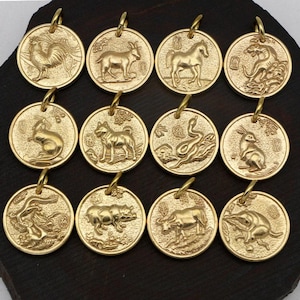 May include: A set of twelve gold-coloured pendants, each depicting an animal from the Chinese zodiac. The circular pendants have a loop for hanging. Animals include a rooster, goat, horse, tiger, rat, dog, snake, rabbit, dragon, pig, ox, and a rat.