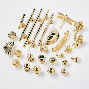 Könnte beinhalten: Eine Sammlung an goldfarbenen Schrankbeschlägen, darunter Griffe, Knöpfe und dekorative Akzente. Die Beschläge zeichnen sich durch eine Vielzahl von Stilen aus, darunter traditionell, modern und verspielt.