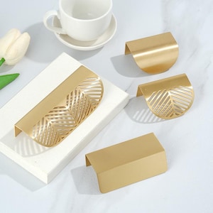 May include: Four gold-toned cabinet drawer pulls. Two of the pulls feature a leaf design, and two are solid gold.