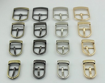 Könnte beinhalten: Ein Satz von 18 Metallschnallen in vier verschiedenen Ausführungen: Antikmessing, Schwarznickel, Silber und Gold. Die Schnallen sind alle gleich groß und haben die gleiche Form, mit einem rechteckigen Rahmen und einer gebogenen, offenen Zunge.