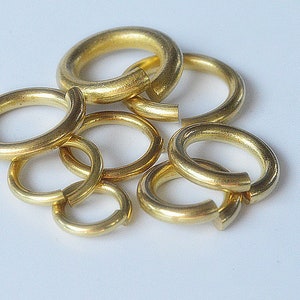 May include: A group of six gold jump rings of varying sizes. The rings are made of metal and are used for connecting jewelry pieces.