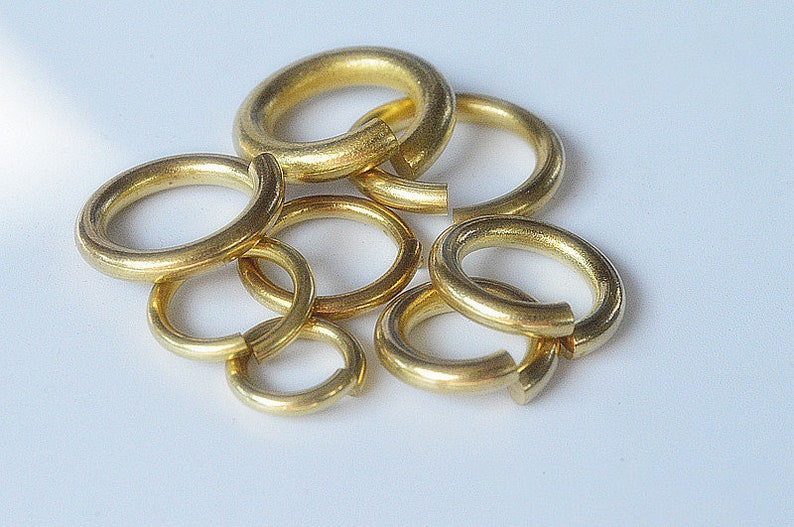 May include: A group of six gold jump rings of varying sizes. The rings are made of metal and are used for connecting jewelry pieces.
